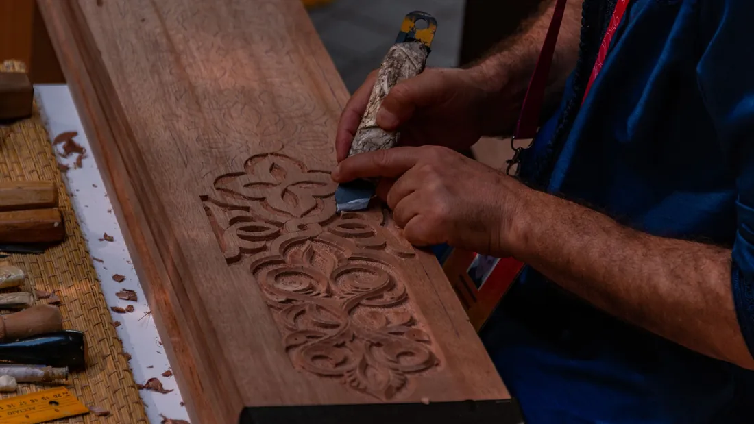 Panel de madera con ornamento floral en relieve mientras se rebaja con una gubia sobre el banco de trabajo
